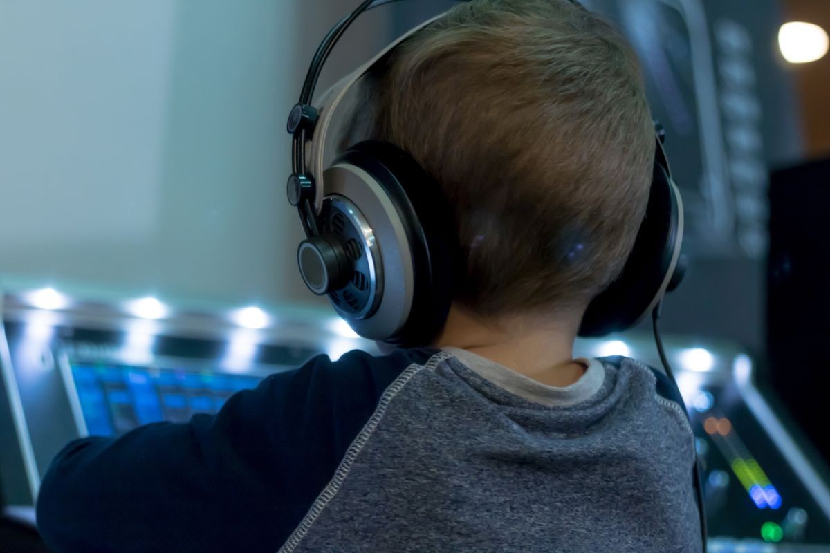 Rear view of kid with headphones playing music at DJ mixete in recording studio. 